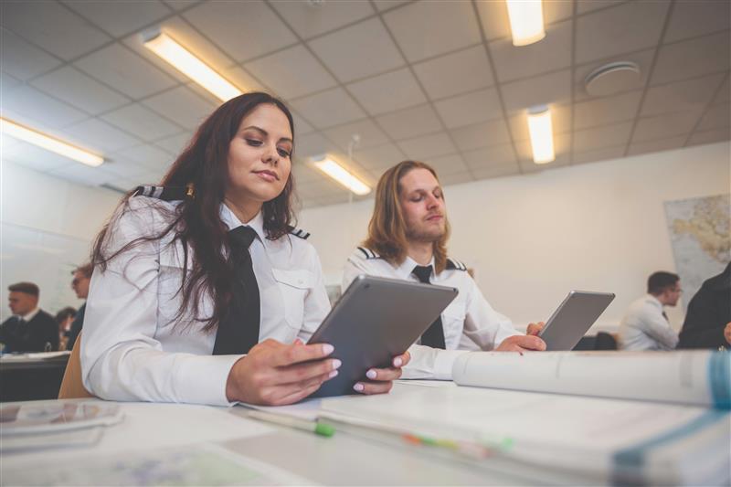 Two people sitting at desks looking at iPads in a classroom.